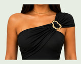 Body asimétrico negro en Licra Amorella con hombro descubierto, drapeado diagonal y detalle dorado.